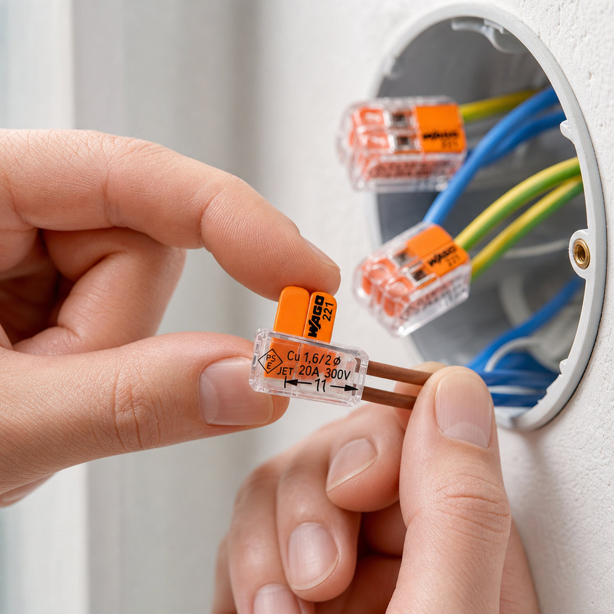 WAGO 221 lever wire connectors – an electrician's hands using the lever connector to join two copper wires inside an open wall junction box