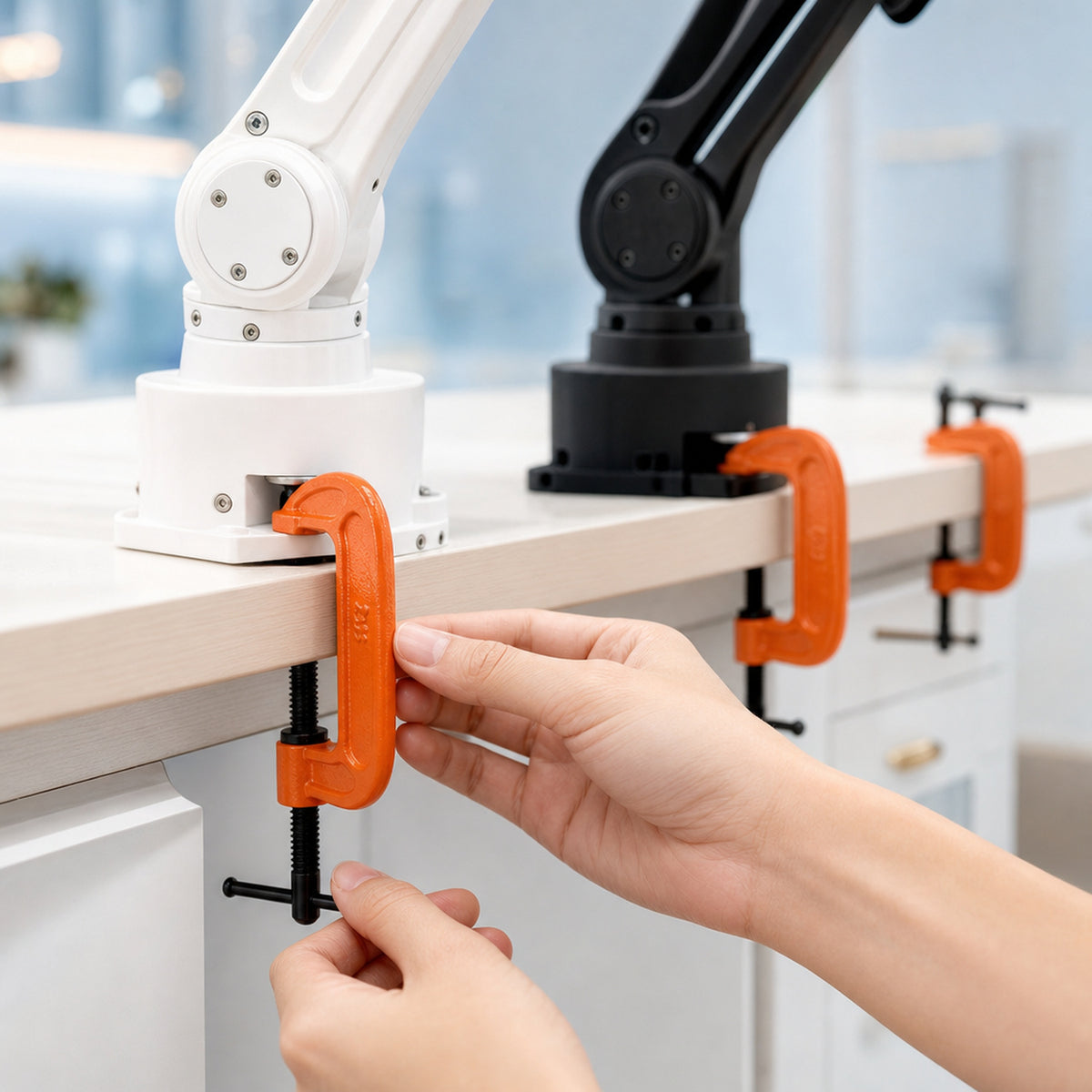 Heavy-duty G-clamps – four orange G-clamps fixing the bases of a white and a black 3D-printed robot arm to a desk edge