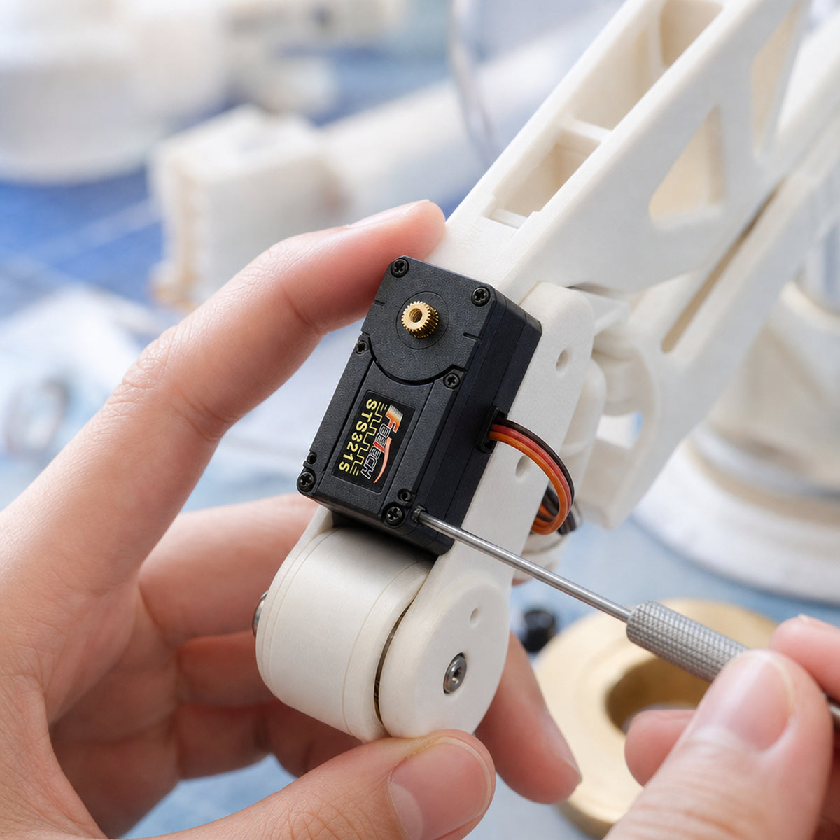 Feetech STS3215 bus servo – a maker's hands screwing the servo into a white 3D-printed robot arm joint on a desk