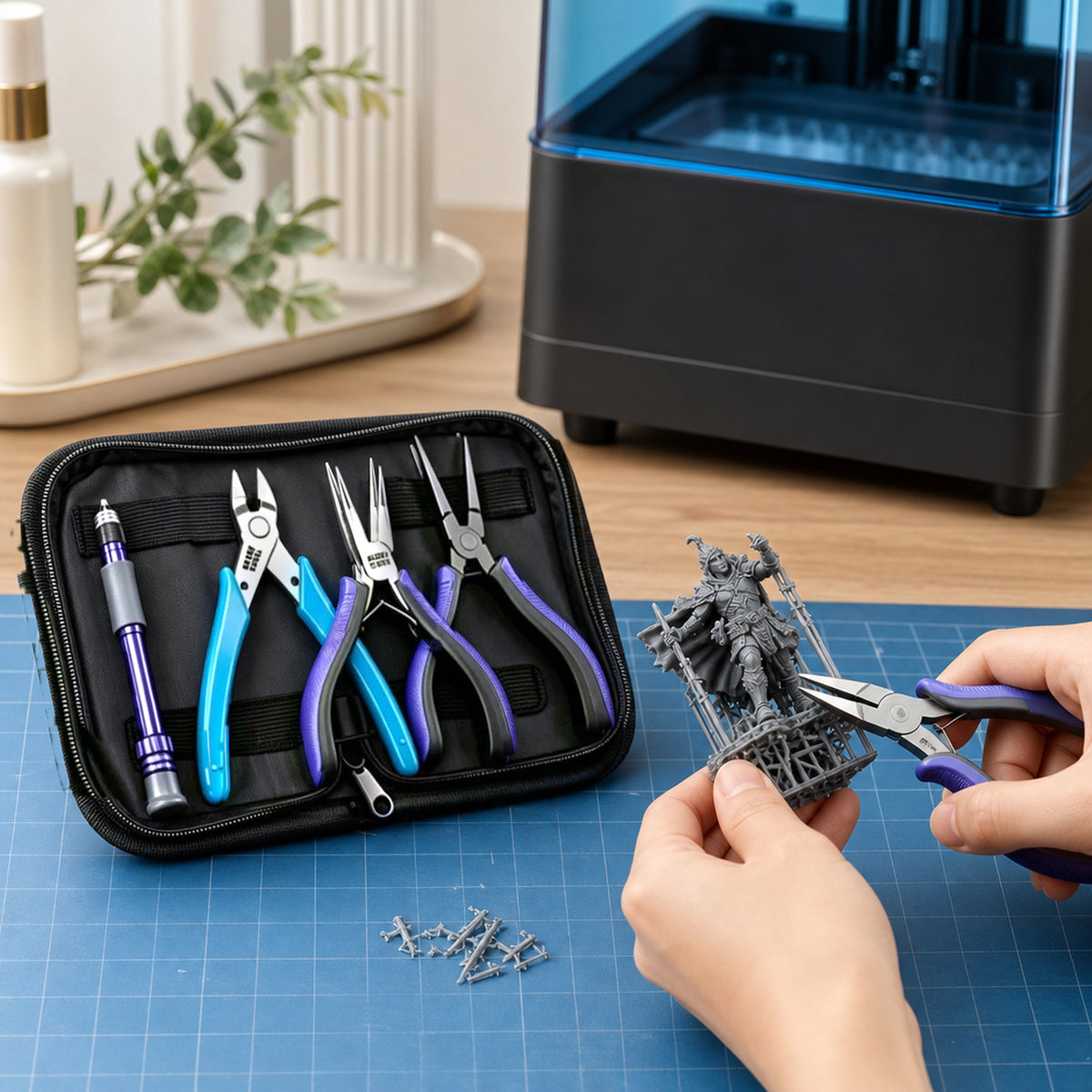 3D print finishing tool kit – hands using the flat-nose pliers to pull a tree support off a freshly printed resin miniature on a desk next to a 3D printer