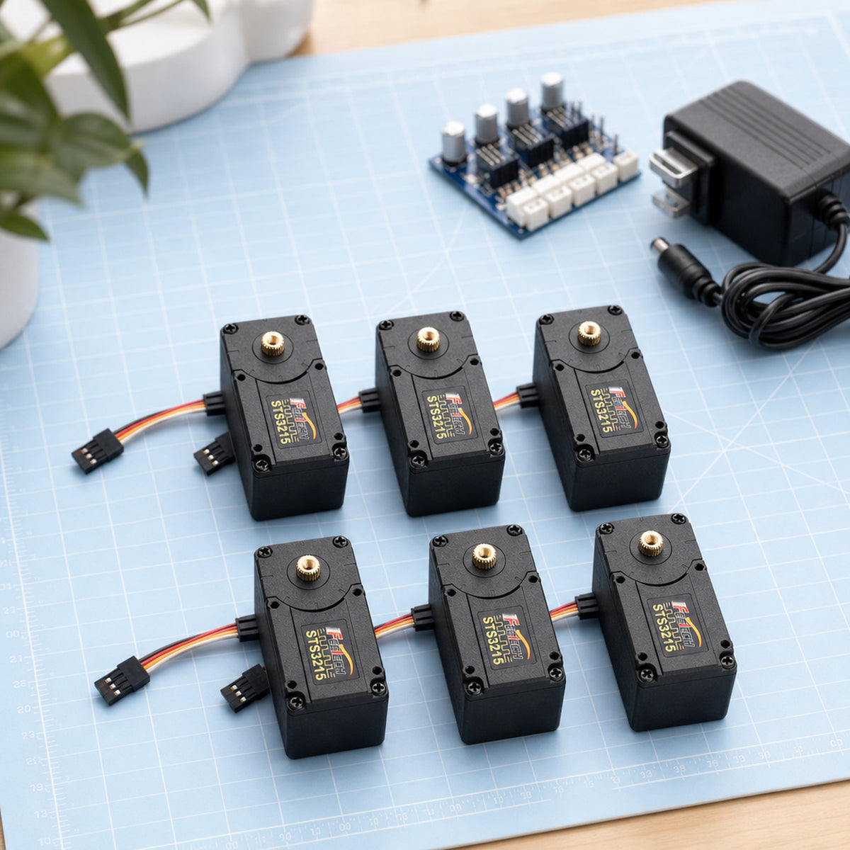 Feetech STS3215 bus servo – six servos laid out on a cutting mat next to a small servo driver board and a 12 V power adapter