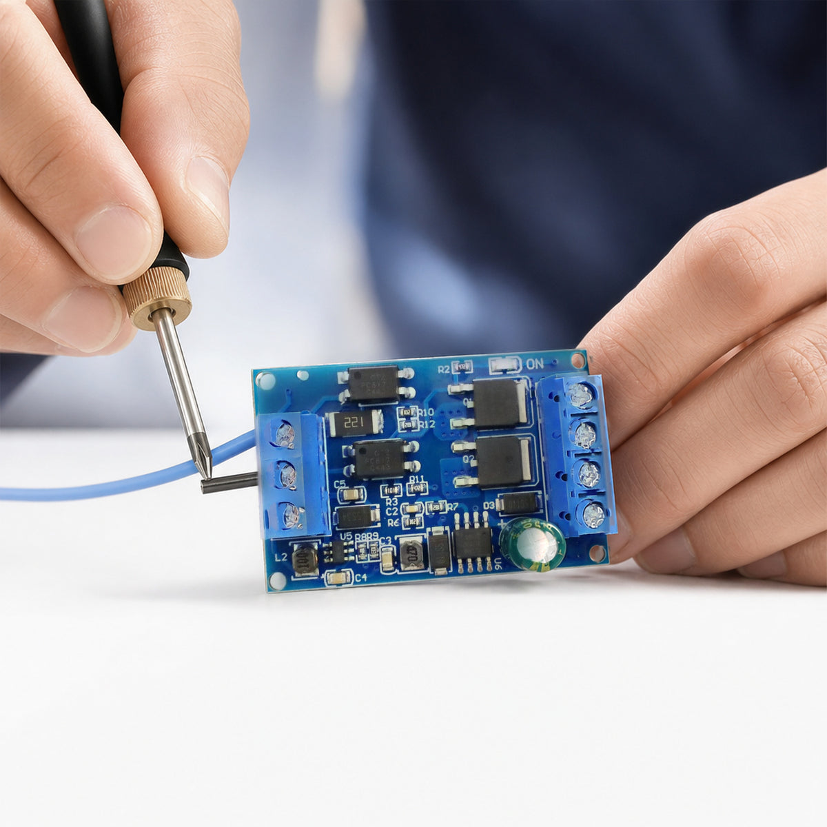 MOSFET PWM switch module – close-up of a maker's hands tightening a wire into the module's blue screw terminal with a small screwdriver