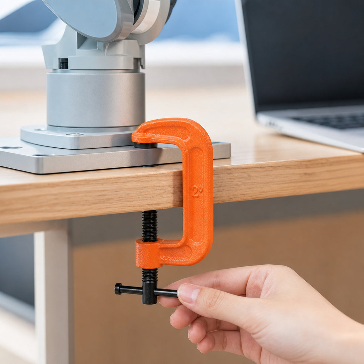 Heavy-duty G-clamps – close-up of one clamp holding a robot arm base plate to a wooden desk